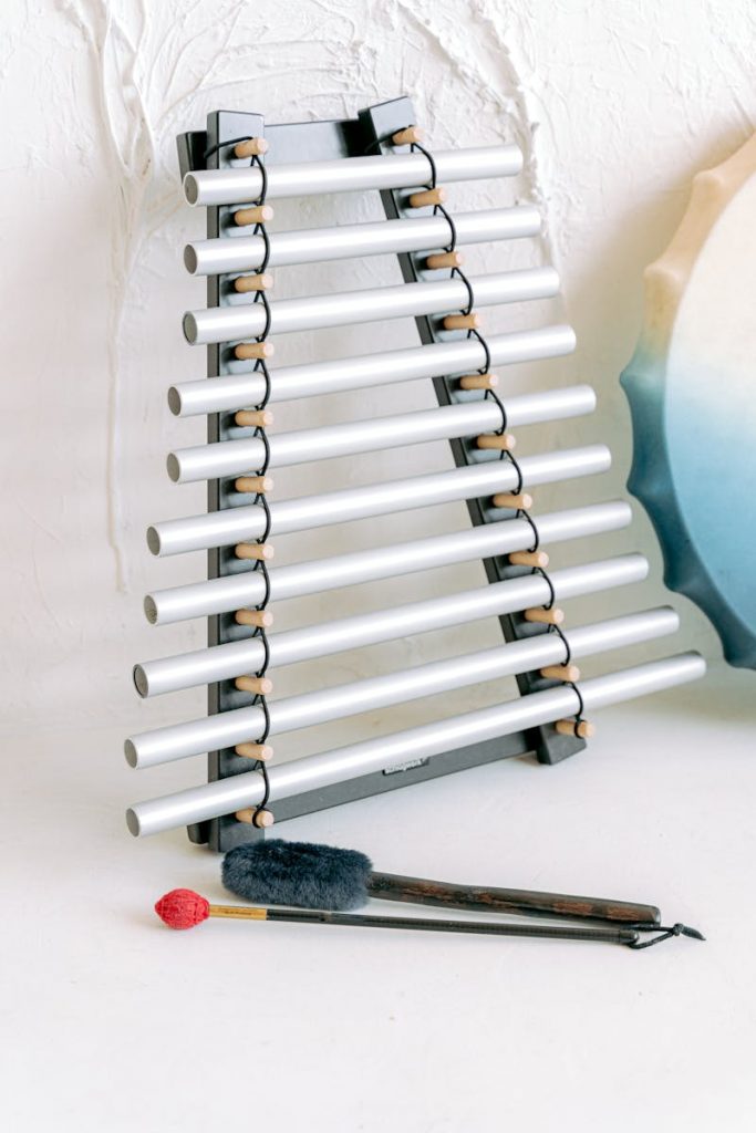 Close-up of percussion instruments, including a chime set and drumsticks, on a textured wall background.